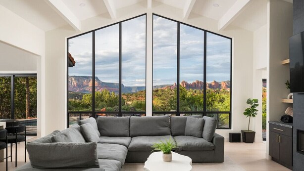 Uma sala de estar moderna com um sofá seccional, uma mesa de centro e uma grande janela com vista para uma paisagem de cânion.