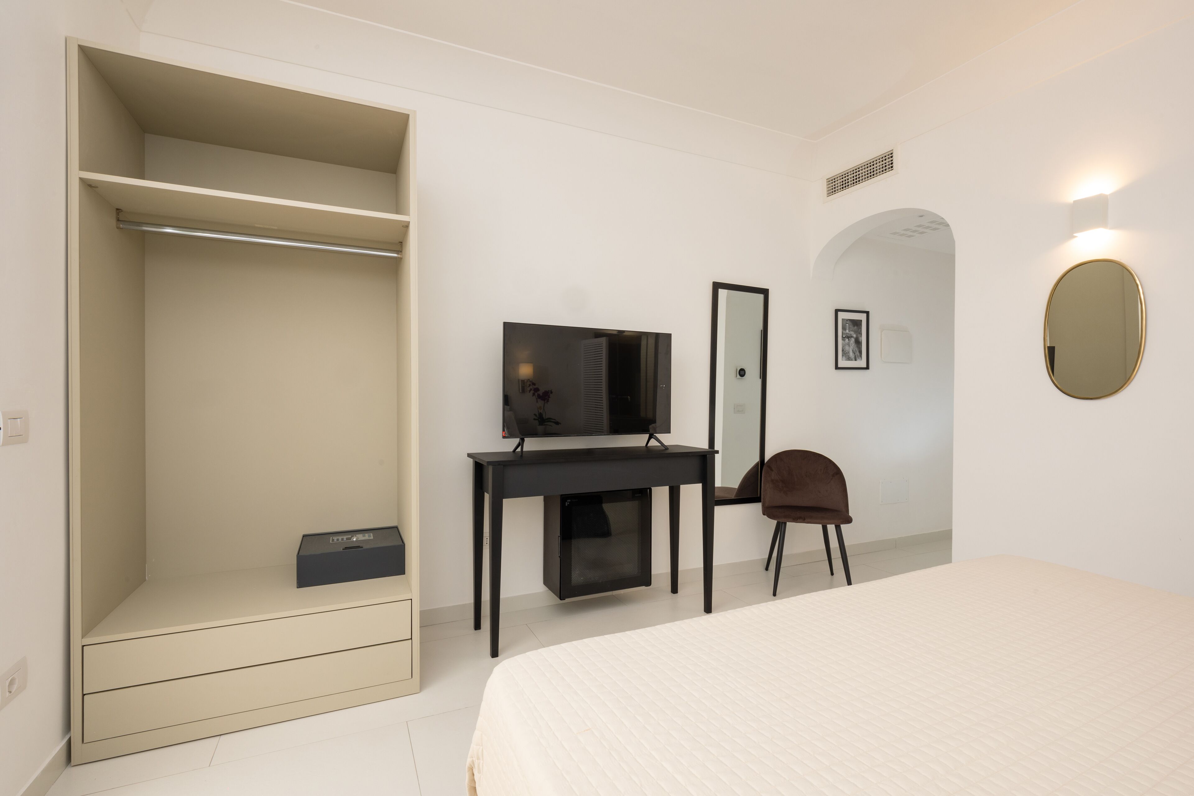 Une chambre à coucher avec un lit, un bureau avec un ordinateur, une chaise, une armoire, un téléviseur, un miroir et un tableau accroché au mur.