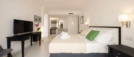 Habitación de hotel con cama, escritorio, televisor y baño a la vista.