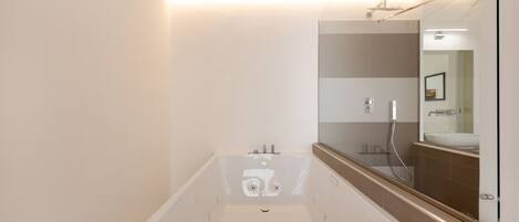 A modern bathroom with a large bathtub, a mirror, and a shower area.