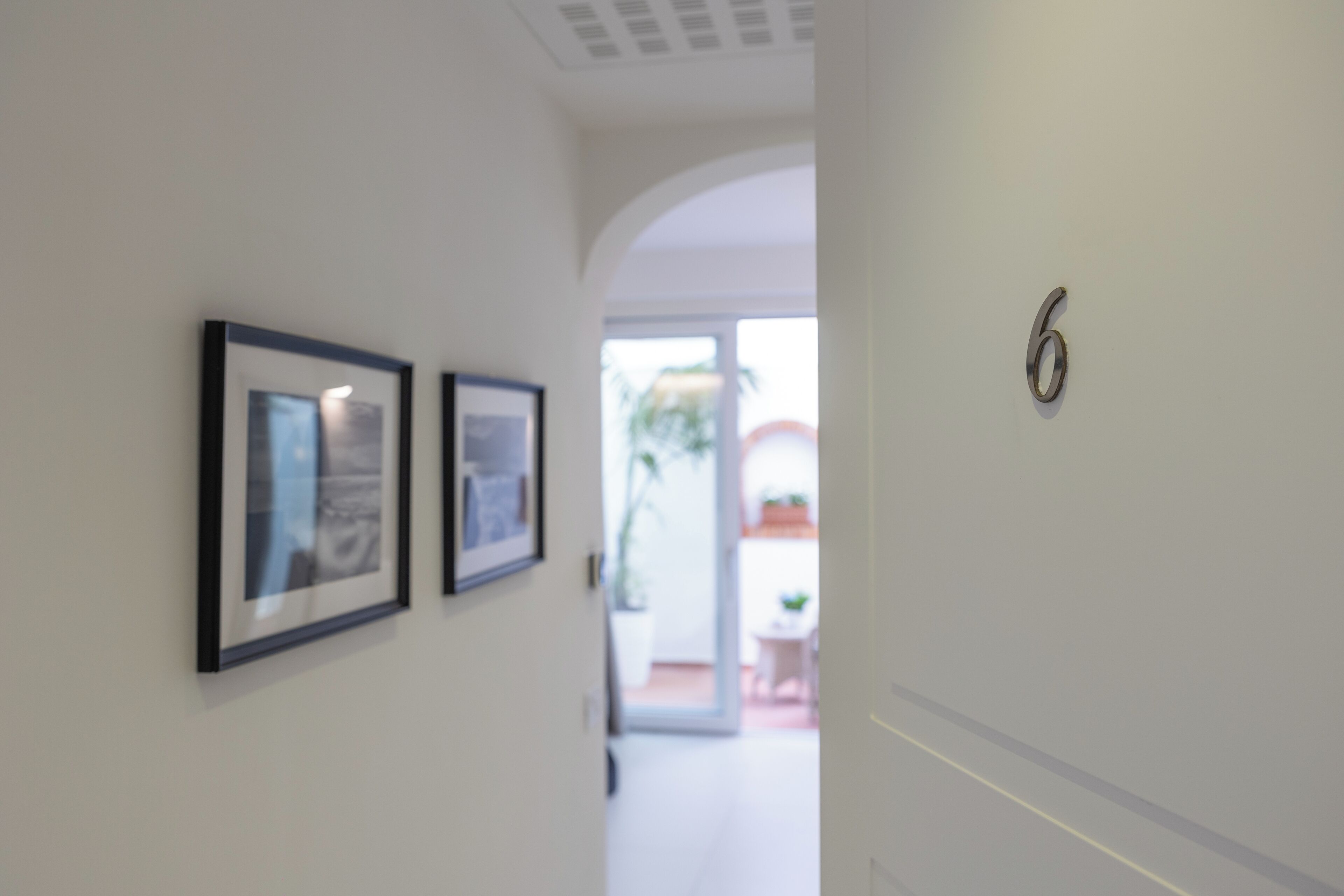 Un couloir avec des tableaux encadrés accrochés au mur et une porte portant le numéro 6.