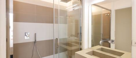 Un baño moderno con cabina de ducha de vidrio, un lavabo color beige y un espejo, además de un perchero visible.