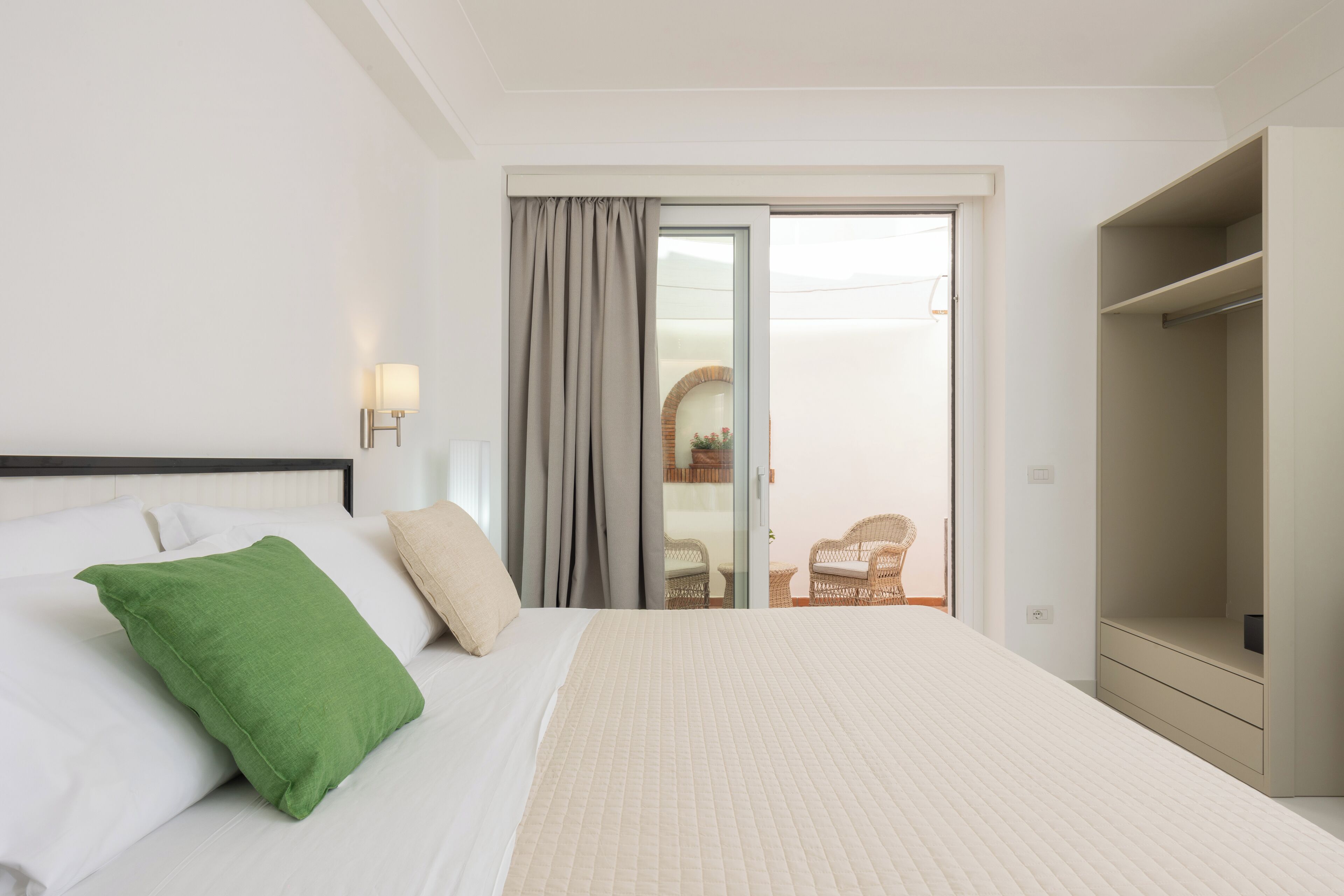 A hotel room with a bed, a wardrobe, a sliding glass door leading to a balcony, and a wall-mounted light fixture.