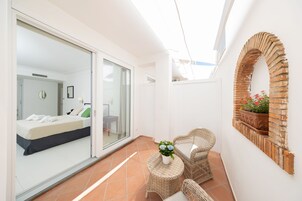 Una habitación moderna con cama, puerta de vidrio que da a otra habitación, mobiliario de mimbre y un arco de ladrillo.
