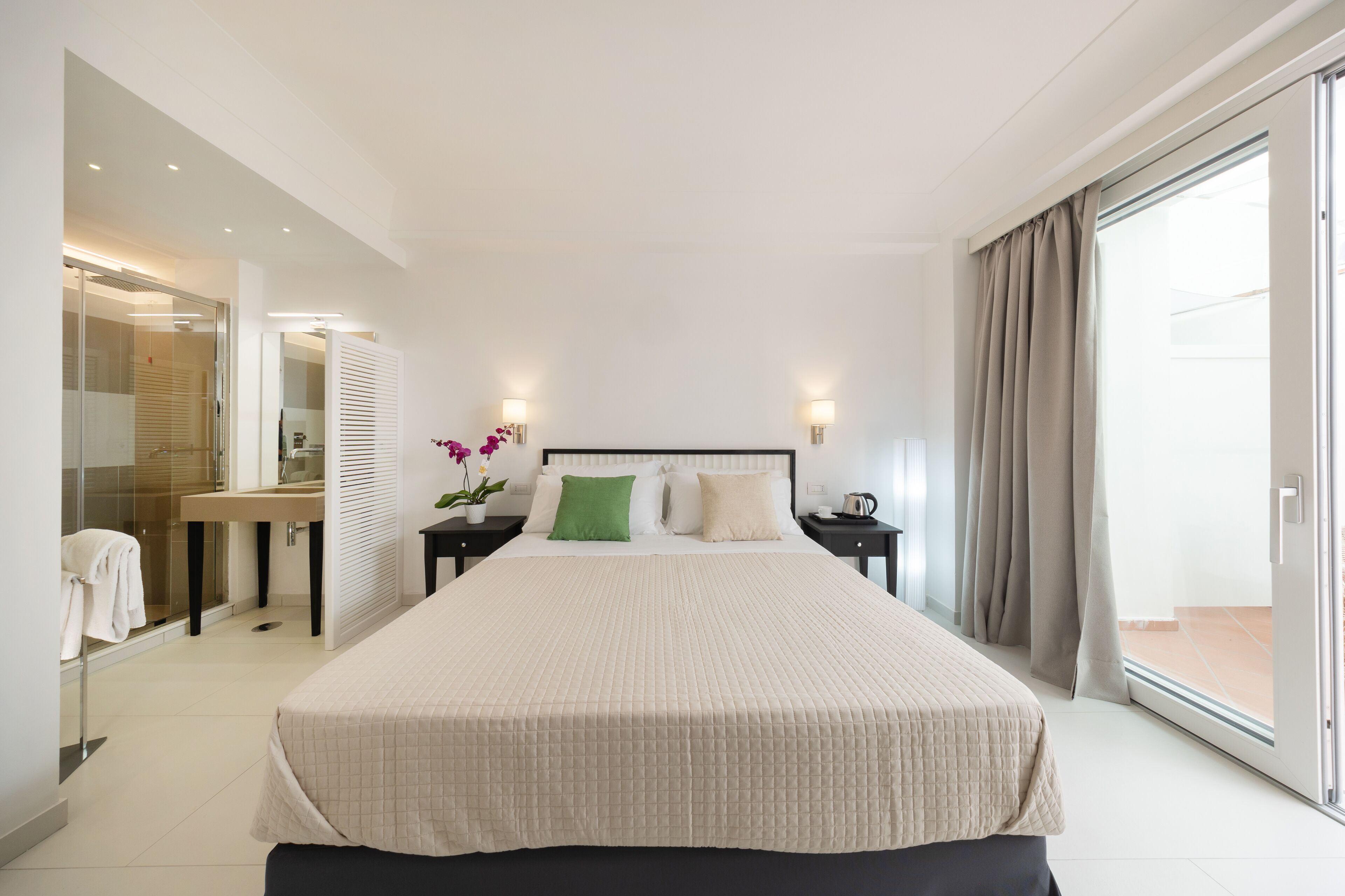 Habitació d'hotel moderna amb un llit gran, un bany amb dutxa de vidre i vistes a través d'una porta corredissa de vidre.