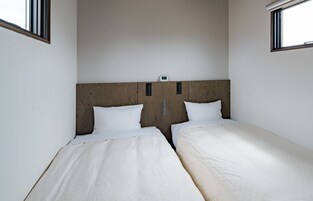 Habitación doble con dos camas individuales, cabecero de madera, ropa de cama blanca y una mesita de noche con lámpara.