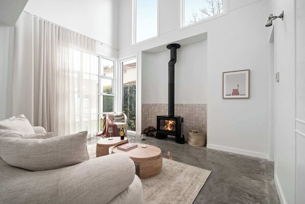 A modern living room with a large window, a fireplace, a sofa, and a coffee table.