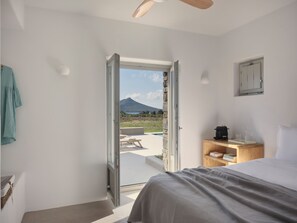Une chambre à coucher avec un lit, une table de chevet, un banc en bois et une vue sur une montagne par une porte ouverte.