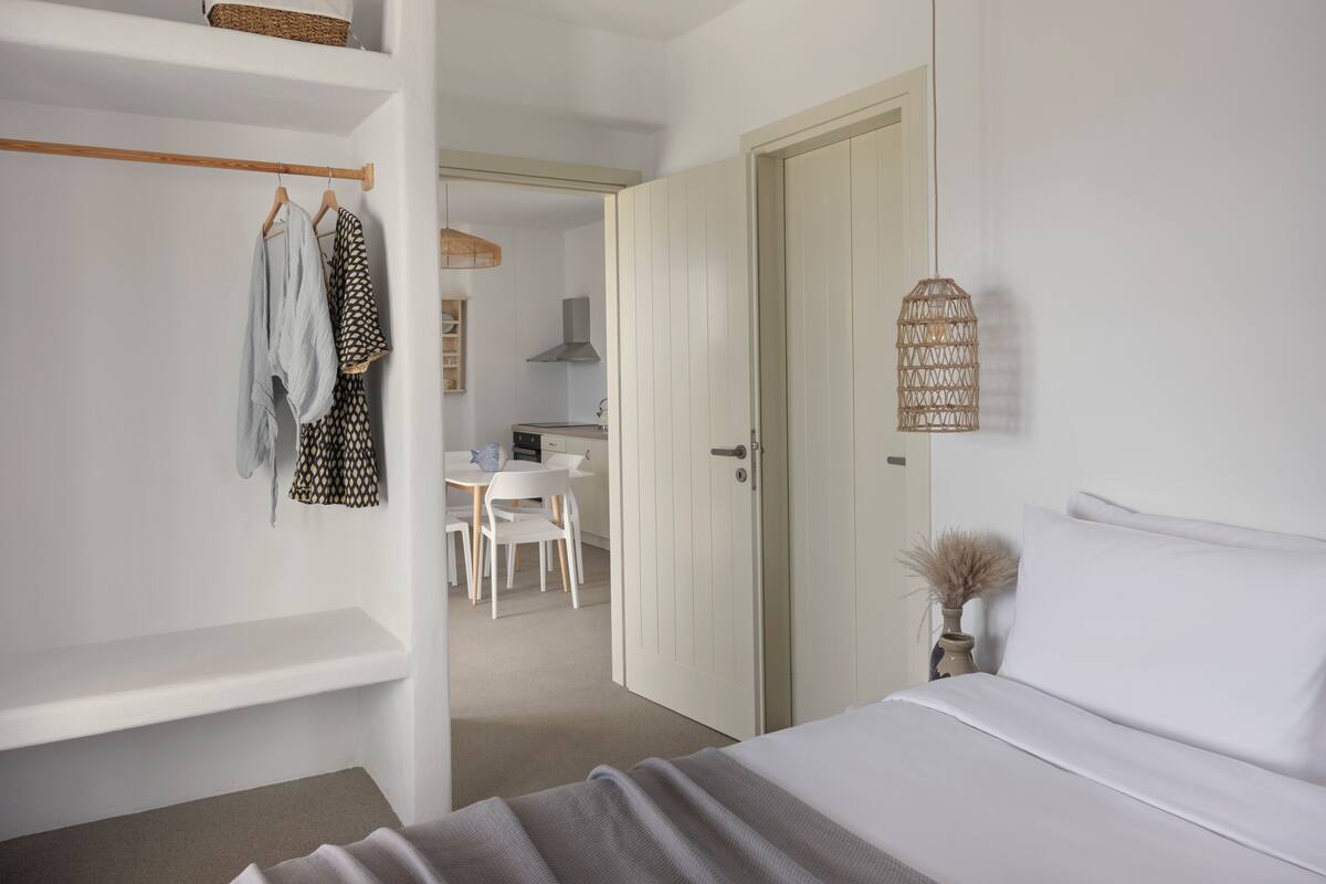Un dormitorio con cama, armario, escritorio y zona de comedor.