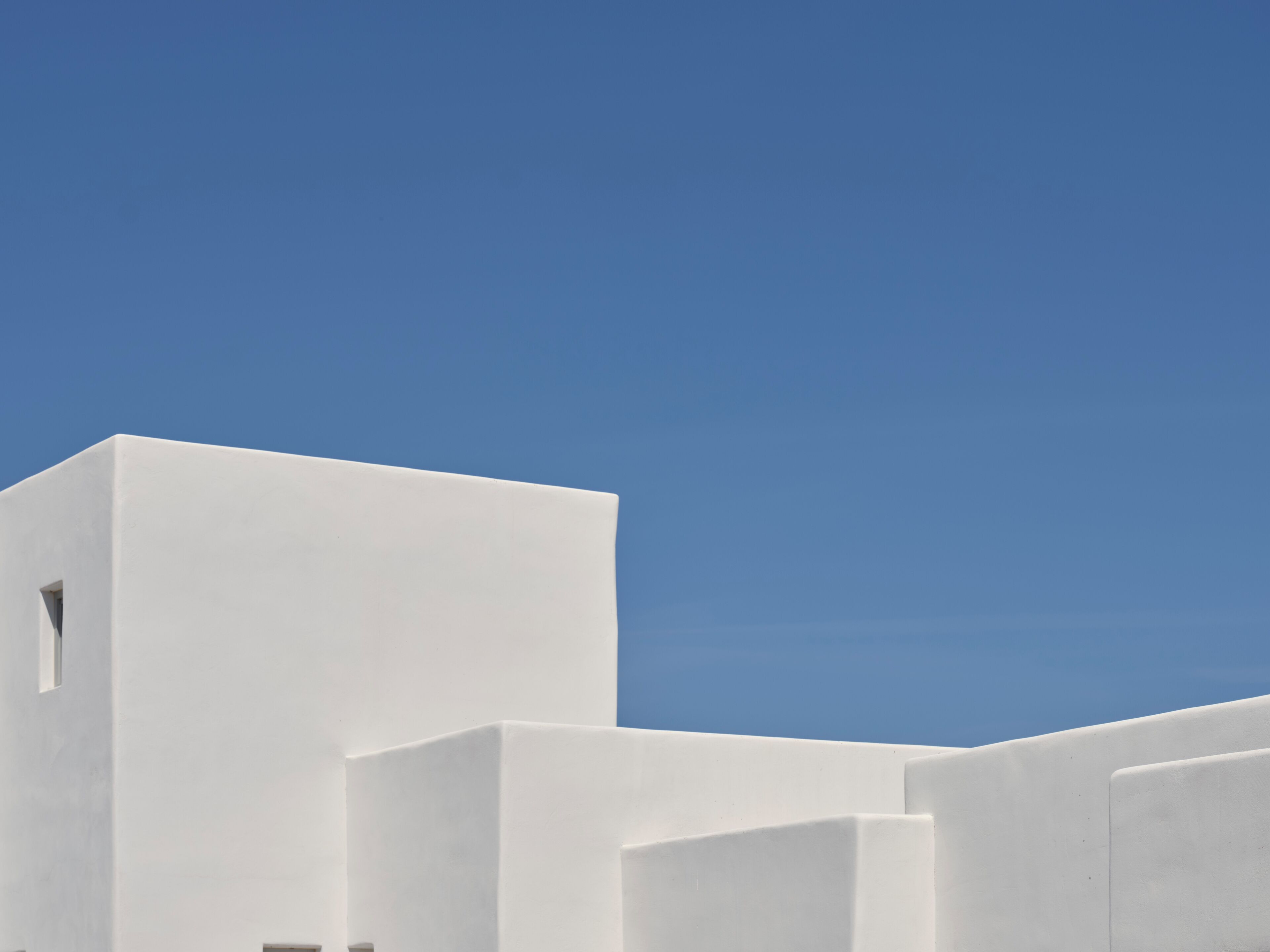 Un edificio moderno con fachada blanca y cielo azul claro al fondo.