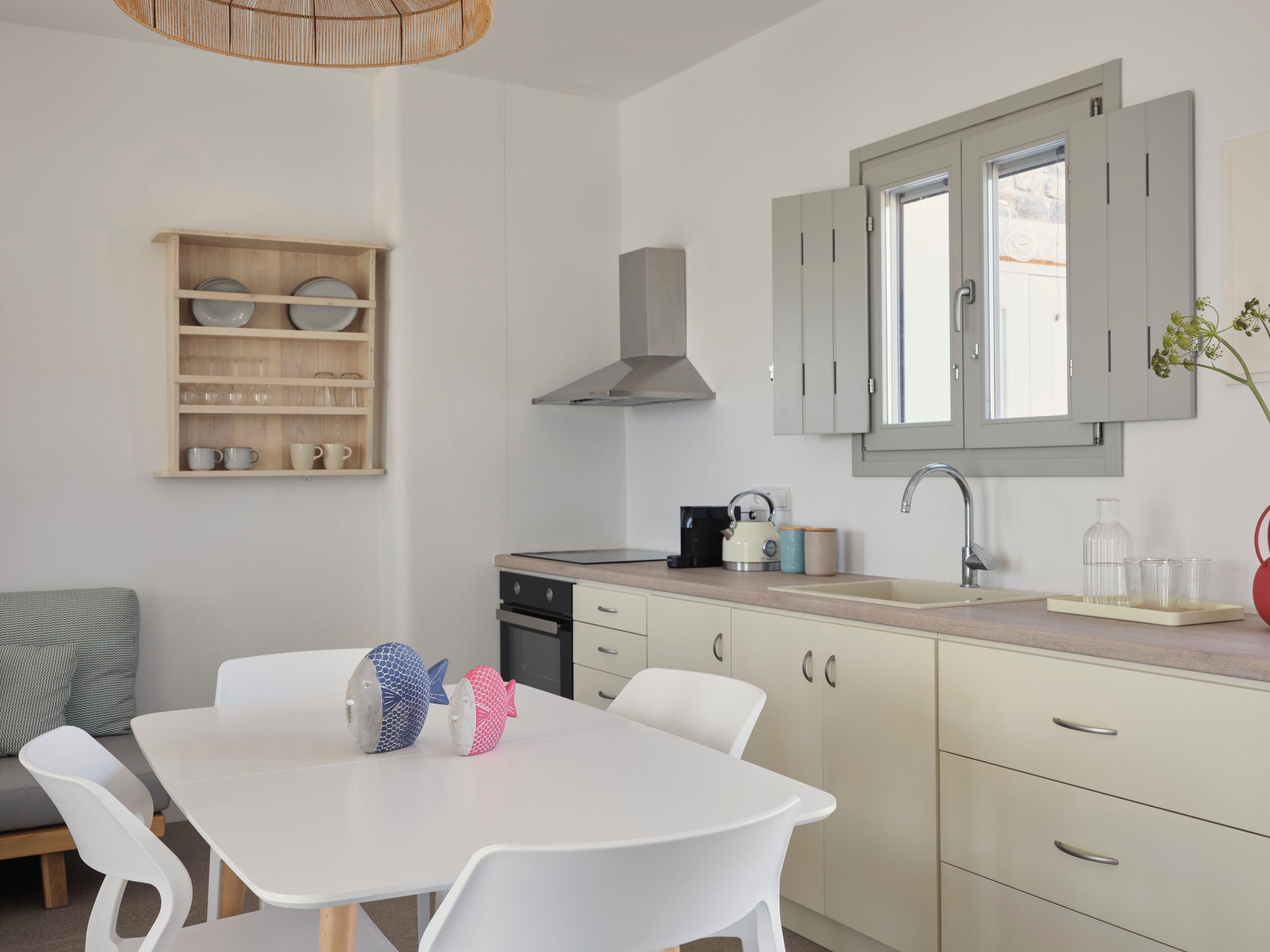 Une cuisine moderne avec des meubles blancs, une cuisinière encastrée et une étagère en bois où sont rangés de la vaisselle.