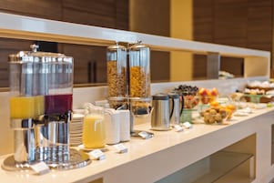 A buffet setup with various food and drink dispensers, including a coffee maker and a fruit bowl.