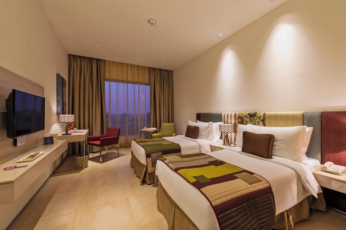 Quarto de hotel com duas camas, televisão, escrivaninha e uma cadeira.