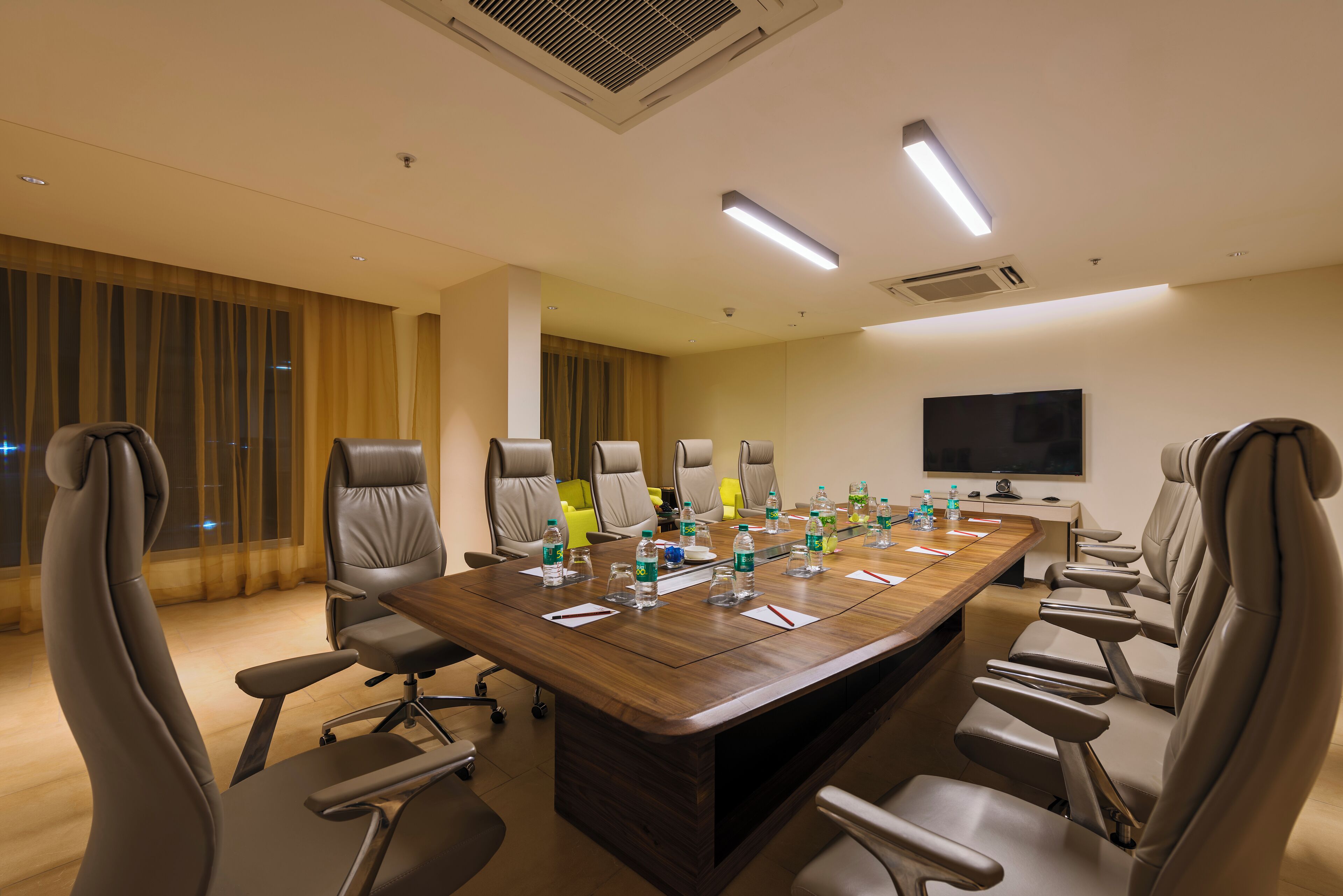 A conference room with a long table, multiple chairs, water bottles, and a flat-screen TV on the wall.
