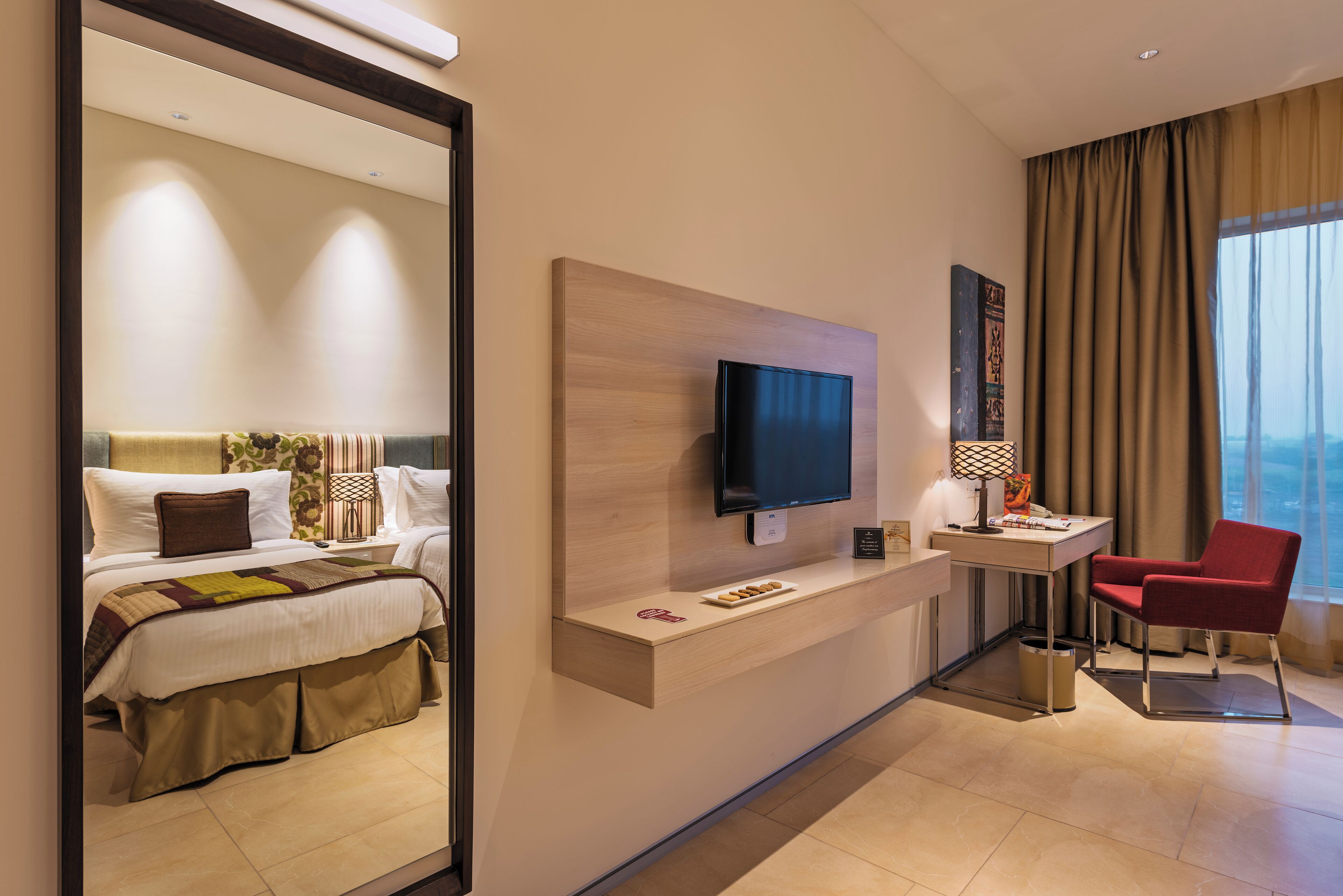A hotel room with a bed, a desk with a TV, a chair, and a large window.