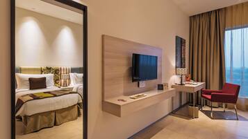 A hotel room with a bed, a desk with a TV, a chair, and a large window.