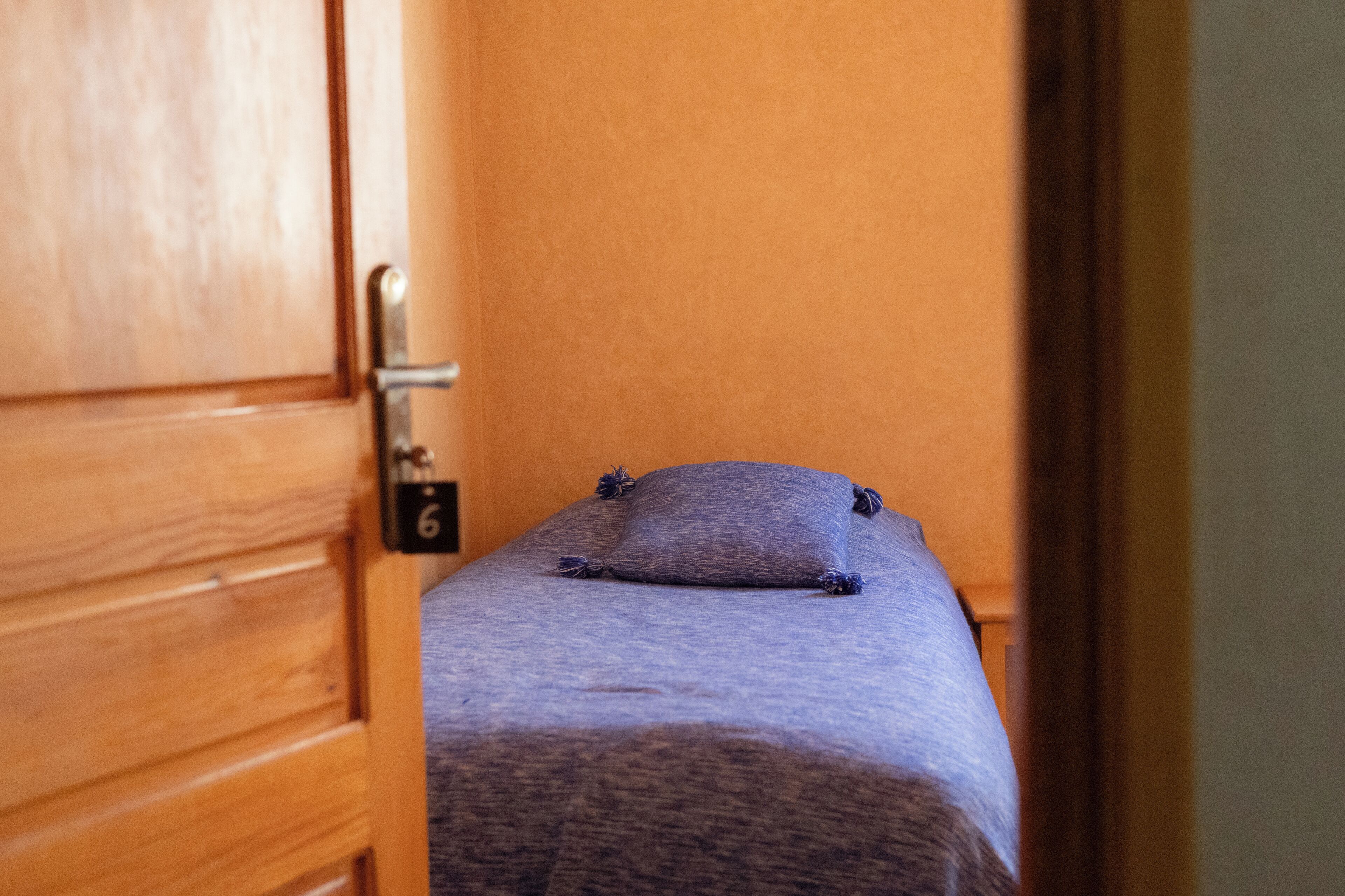 A small, single-bed room with a wooden door and a number '6' on it.