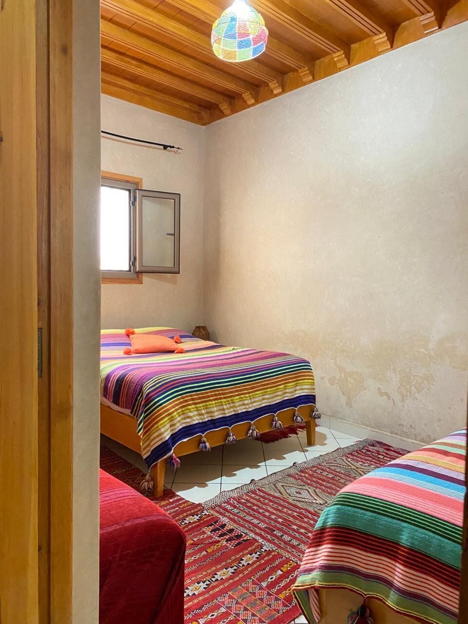 Una camera da letto con due letti, soffitto in legno, una finestra e un lampadario colorato.