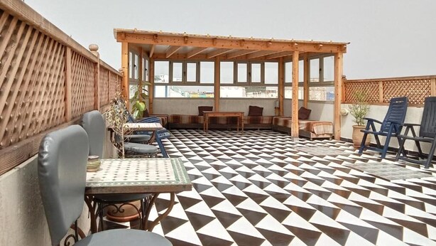 An outdoor patio with a geometric patterned floor, a wooden pergola, and seating arrangements. - Riad Essaouira (Essaouira)