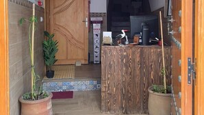 A wooden reception desk with a tiled floor, a wooden door, and potted plants. - Riad Essaouira (Essaouira)