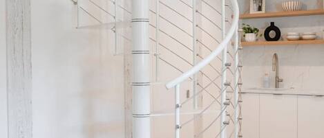 A modern spiral staircase with a minimalist design, white railings, and a wooden floor.