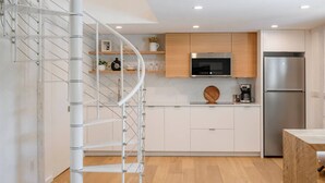 A modern kitchen with white cabinets, a built-in oven, a stainless steel refrigerator, and a spiral staircase.