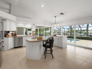 A modern kitchen with white cabinetry, a central island, and a large window overlooking a swimming pool.