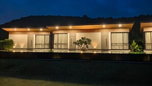 A modern, multi-story residential building with a flat roof, large windows, and a well-lit exterior. - River's Edge By Escape Stays (Nashik)
