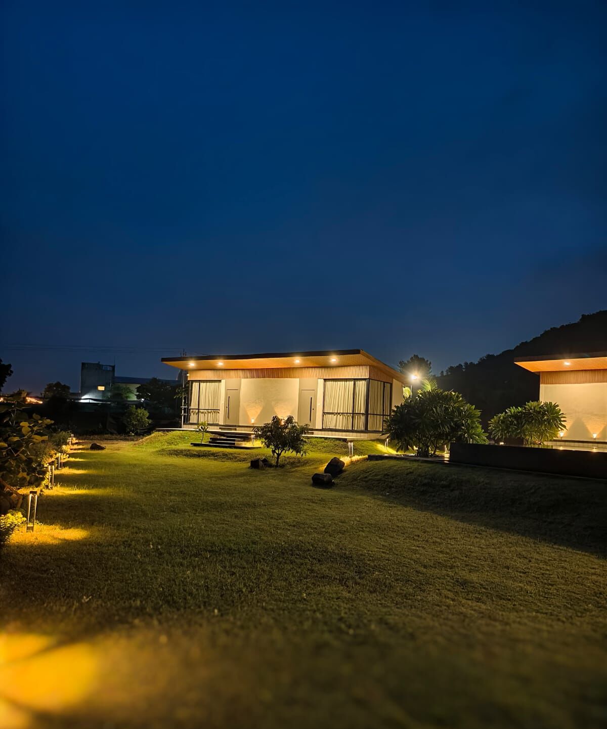 A modern house with a well-lit lawn and a large window.