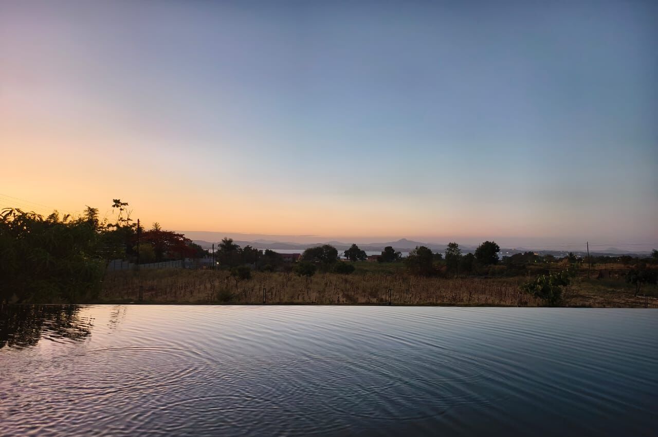 A serene landscape with a calm body of water, trees, and distant mountains under a clear sky.