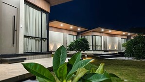 A modern house with a large sliding glass door, a covered patio, and a well-maintained lawn. - River's Edge By Escape Stays (Nashik)