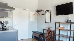 A compact kitchen with a stove, a hanging rack, a small table with a ship model, and a TV on the wall. - triple a Apartments in Altfeld (Marktheidenfeld)