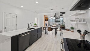 Cozinha moderna com ilha central, sala de jantar com lustre e escadaria para um andar superior.