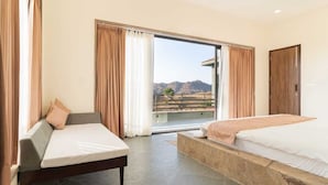 Een hotelkamer met een bed, een slaapbank en een grote schuifdeur naar een balkon met uitzicht op de bergen.