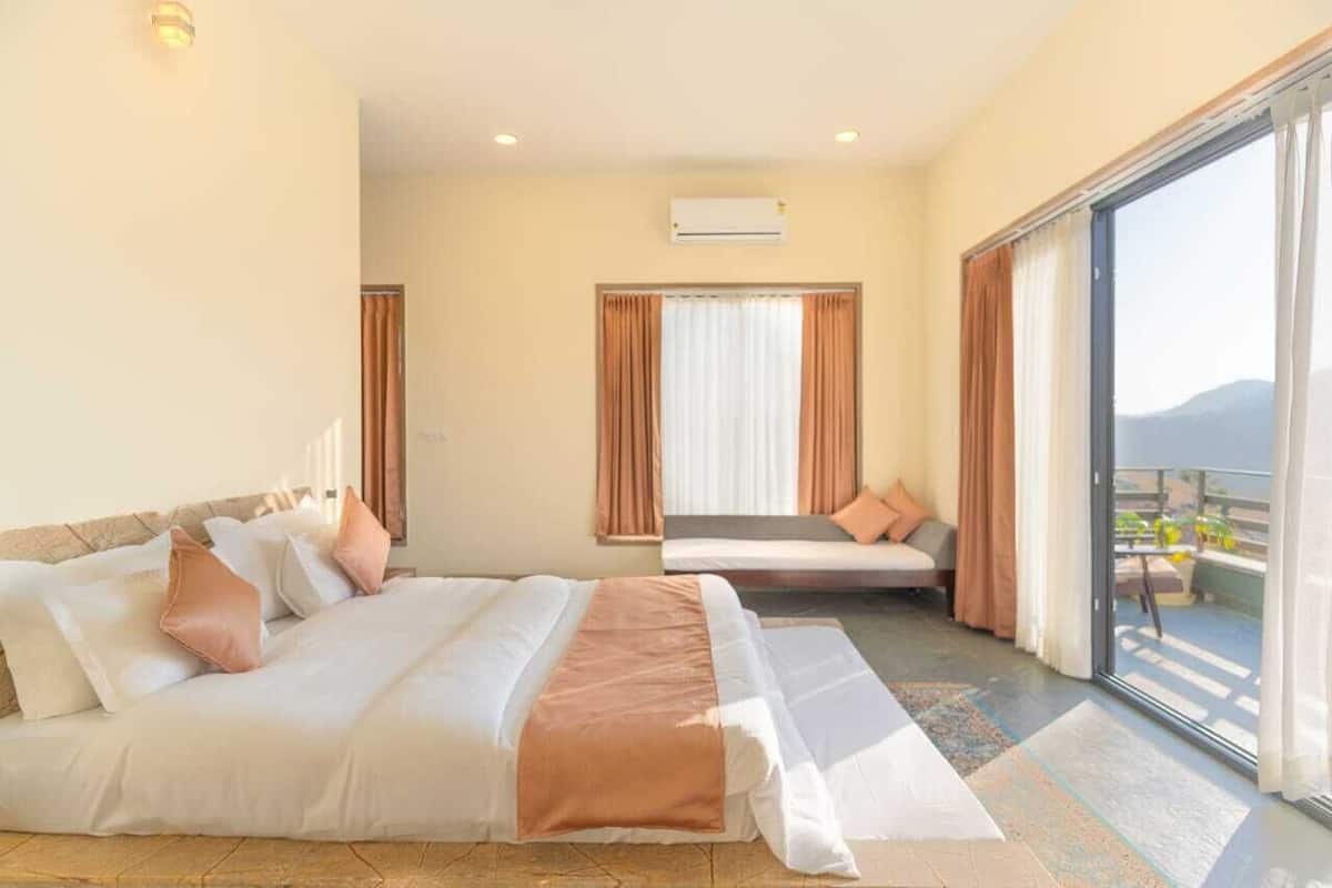 A hotel room with a large bed, a sofa, and a balcony with a view.