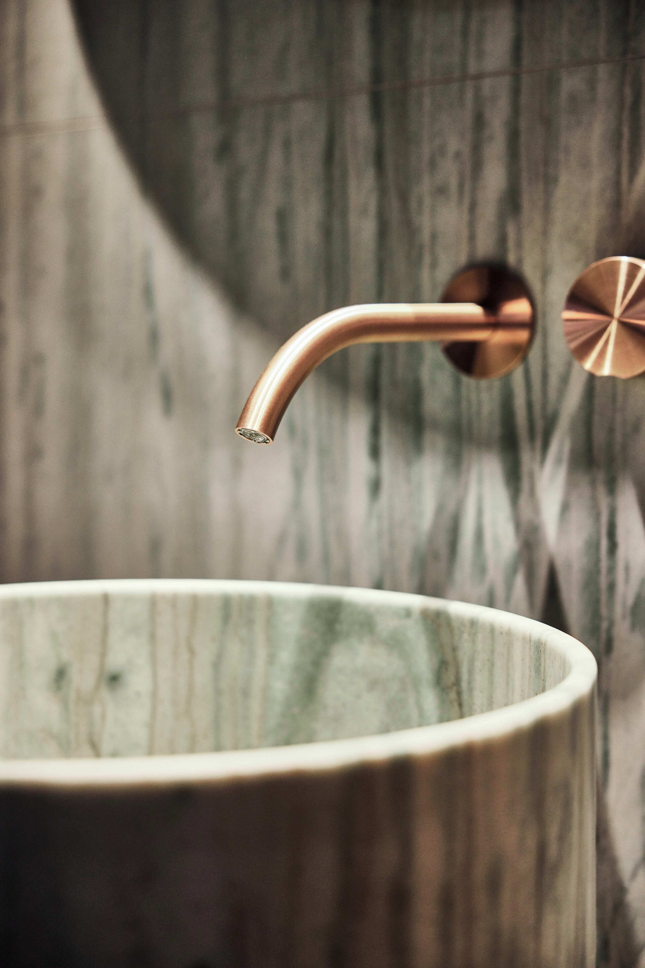 A bathroom with a copper faucet and a ceramic sink.
