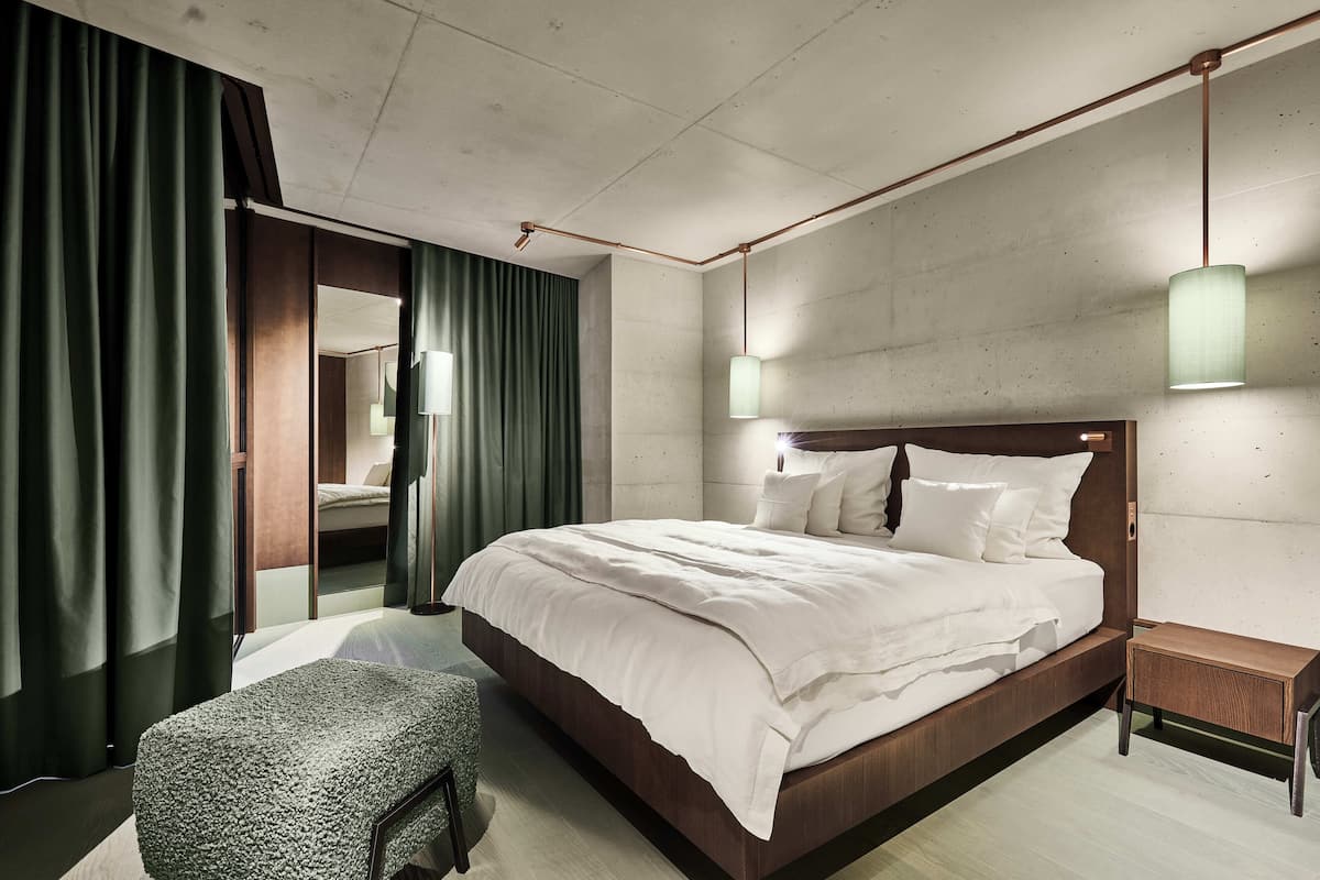 Un dormitorio moderno con una cama grande, una mesita de noche, un banco y un espejo.