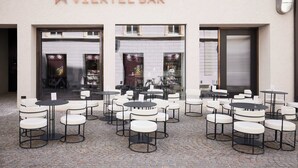 An outdoor seating area with multiple tables and chairs in front of a building labeled "VIERTEL BAR". - Boutique Hotel Badhaus (Bressanone)