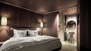 A modern bedroom with a large bed, wooden walls, and a circular mirror. - Boutique Hotel Badhaus (Bressanone)