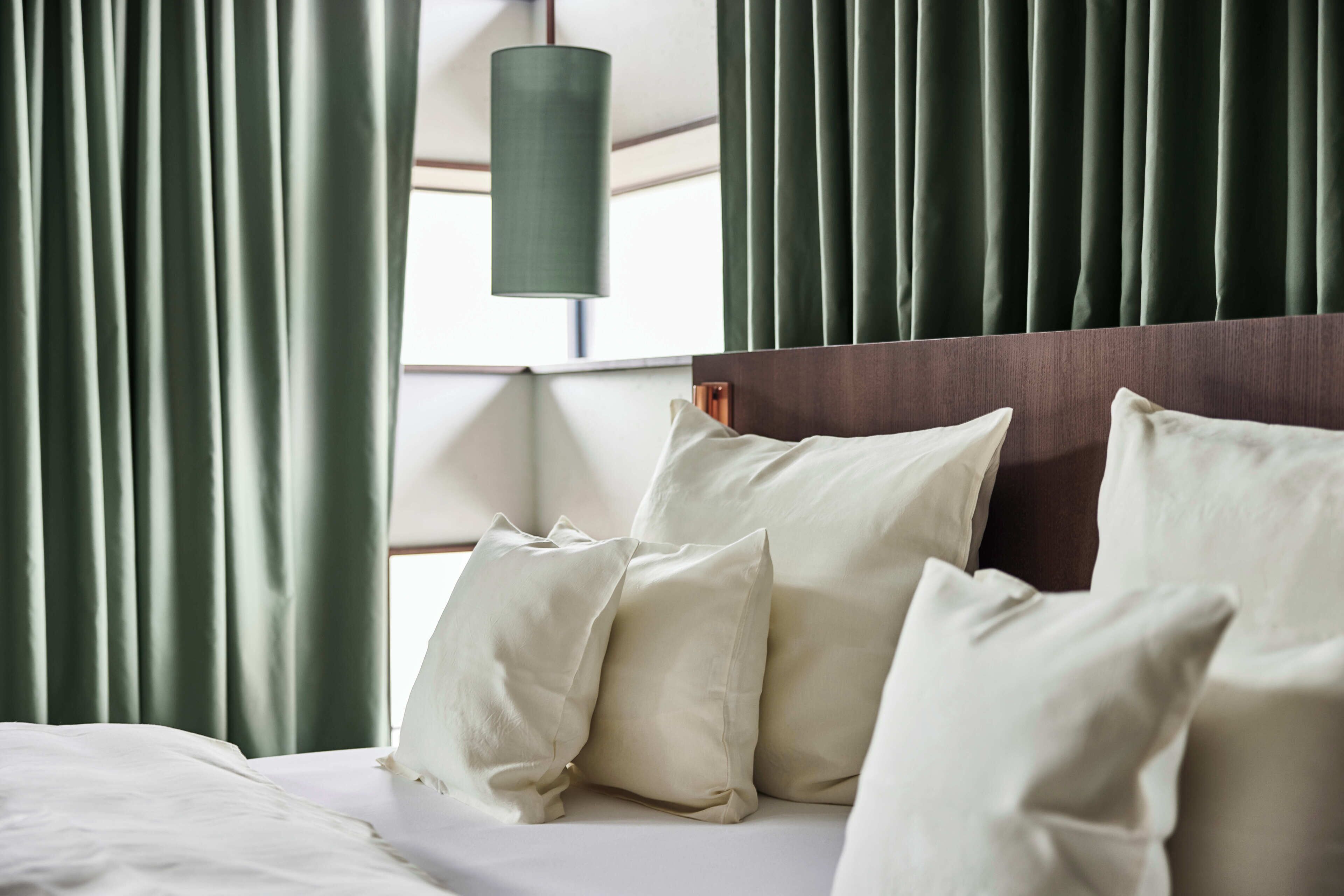 A neatly made bed with white linens and pillows, a wooden headboard, and green curtains.