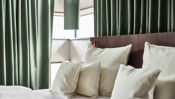 A neatly made bed with white linens and pillows, a wooden headboard, and green curtains.