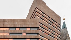 A modern building with a geometric facade and a prominent tower with a spire. - Boutique Hotel Badhaus (Bressanone)