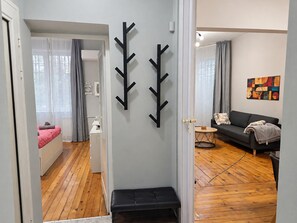 A modern living room with a sofa, a bench, a small round table, and a wall-mounted abstract art piece. - NDK Top Center Sofia Two Bedroom Apartment with ACC (Sofia)