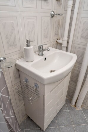 Un baño con lavamanos blanco, un dispensador de papel higiénico y un perchero para toallas.