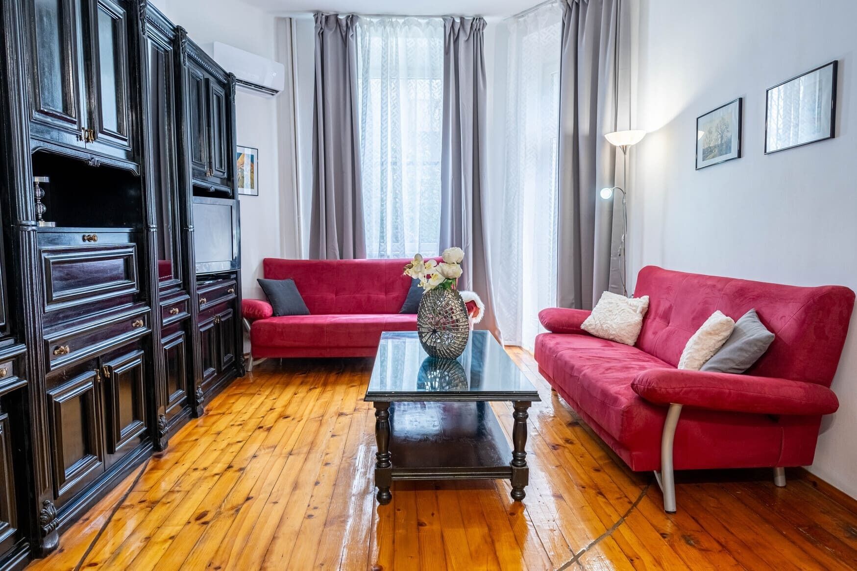 Un salon avec un canapé rouge, une table basse en verre et un meuble en bois foncé.