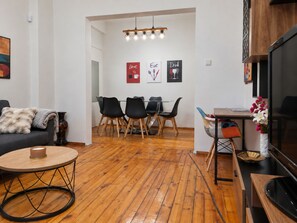 A modern living room with a sofa, a round coffee table, and a dining area with chairs and a table. - NDK Top Center Sofia Two Bedroom Apartment with ACC (Sofia)