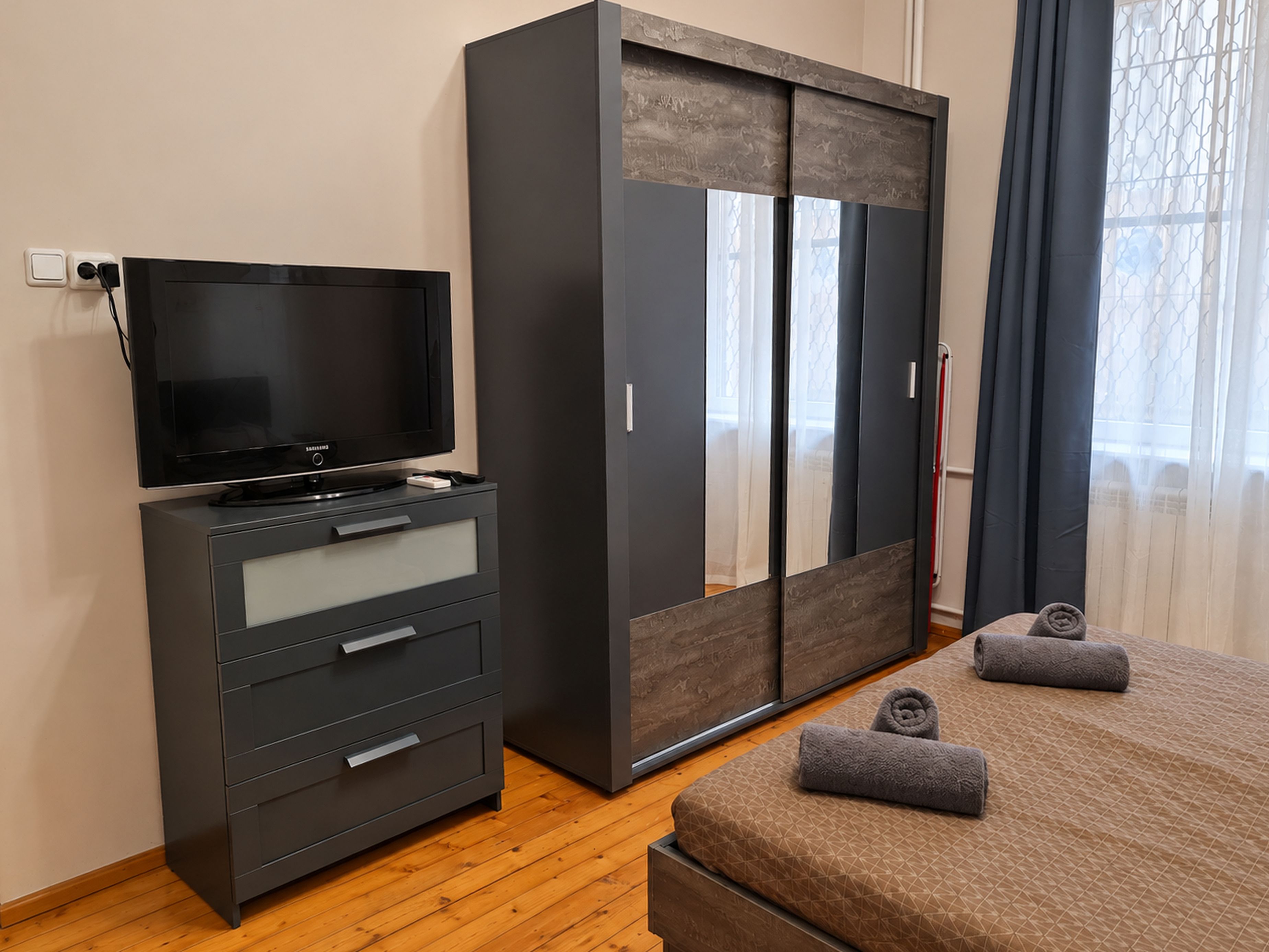 A modern bedroom with a TV, wardrobe, and a bed with towels.
