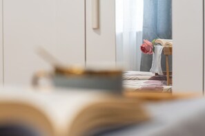 Un dormitorio con cama, una mesita de noche con un libro y una rosa, y una ventana con cortinas.
