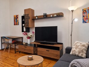 Ein modernes Wohnzimmer mit Flachbildfernseher, Holzmöbeln, einem runden Couchtisch und einer Couch mit einem flauschigen Kissen.