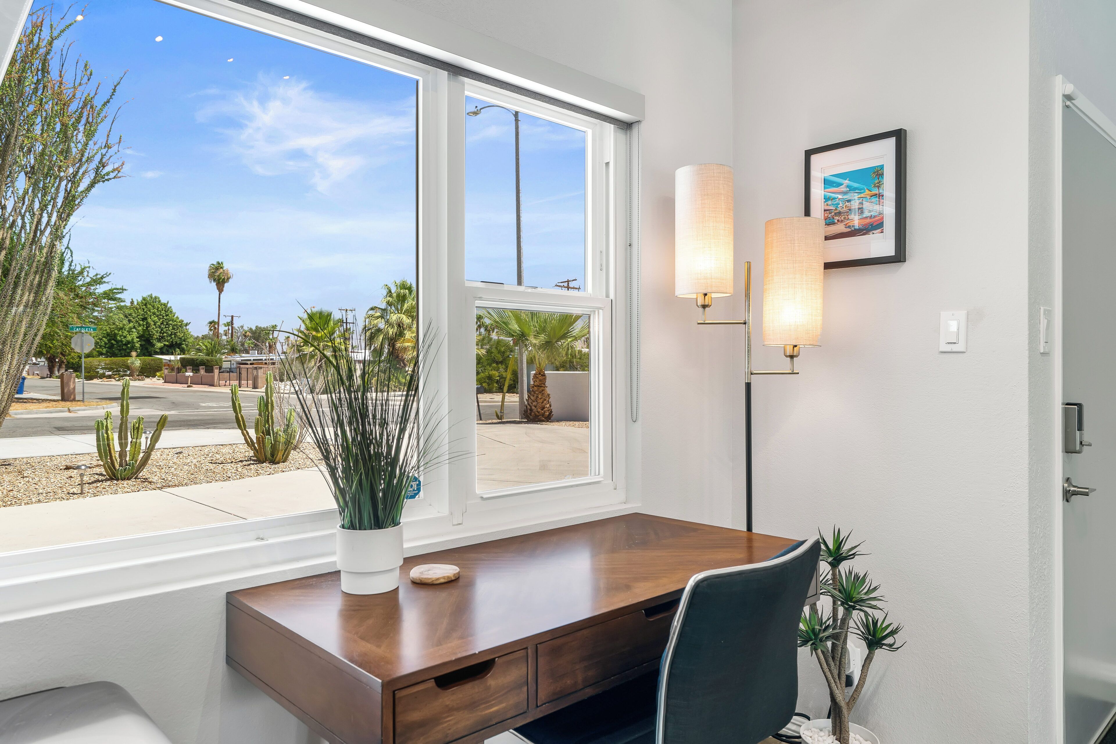 A modern office space with a large window, a wooden desk, a chair, and two wall-mounted lamps.